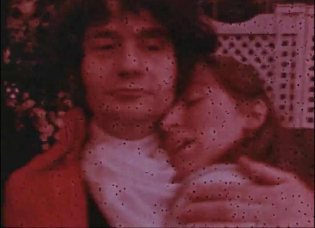 A color film still of a man of a cravat-wearing man embracing a woman.
