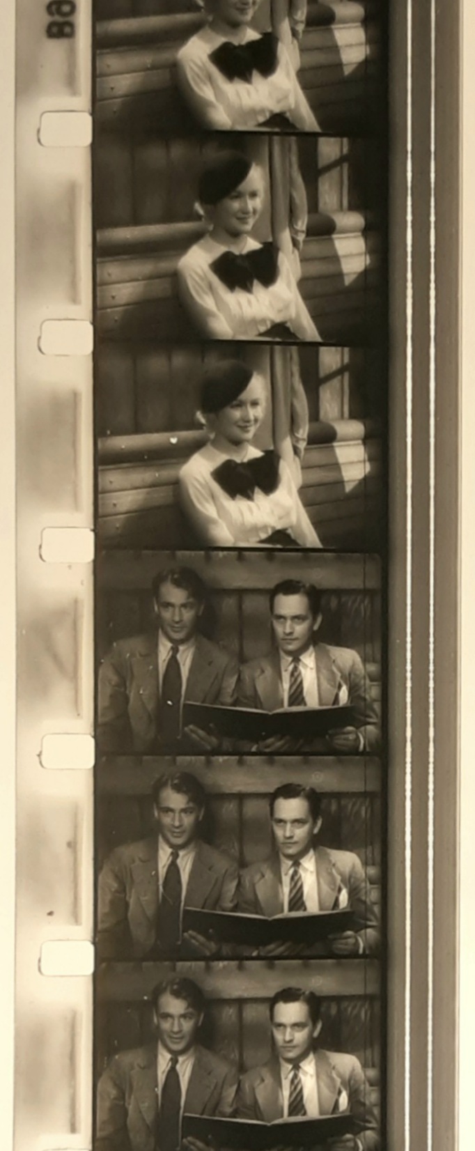 A color photograph of a strip of 16mm film from Design for Living. The top frames show Miriam Hopkins sitting on a train and smiling. The bottom frames show the reverse shot, with Gary Cooper and Frederic March, sitting side-by-side, looking back at Hopkins, with somewhat bemused expressions.