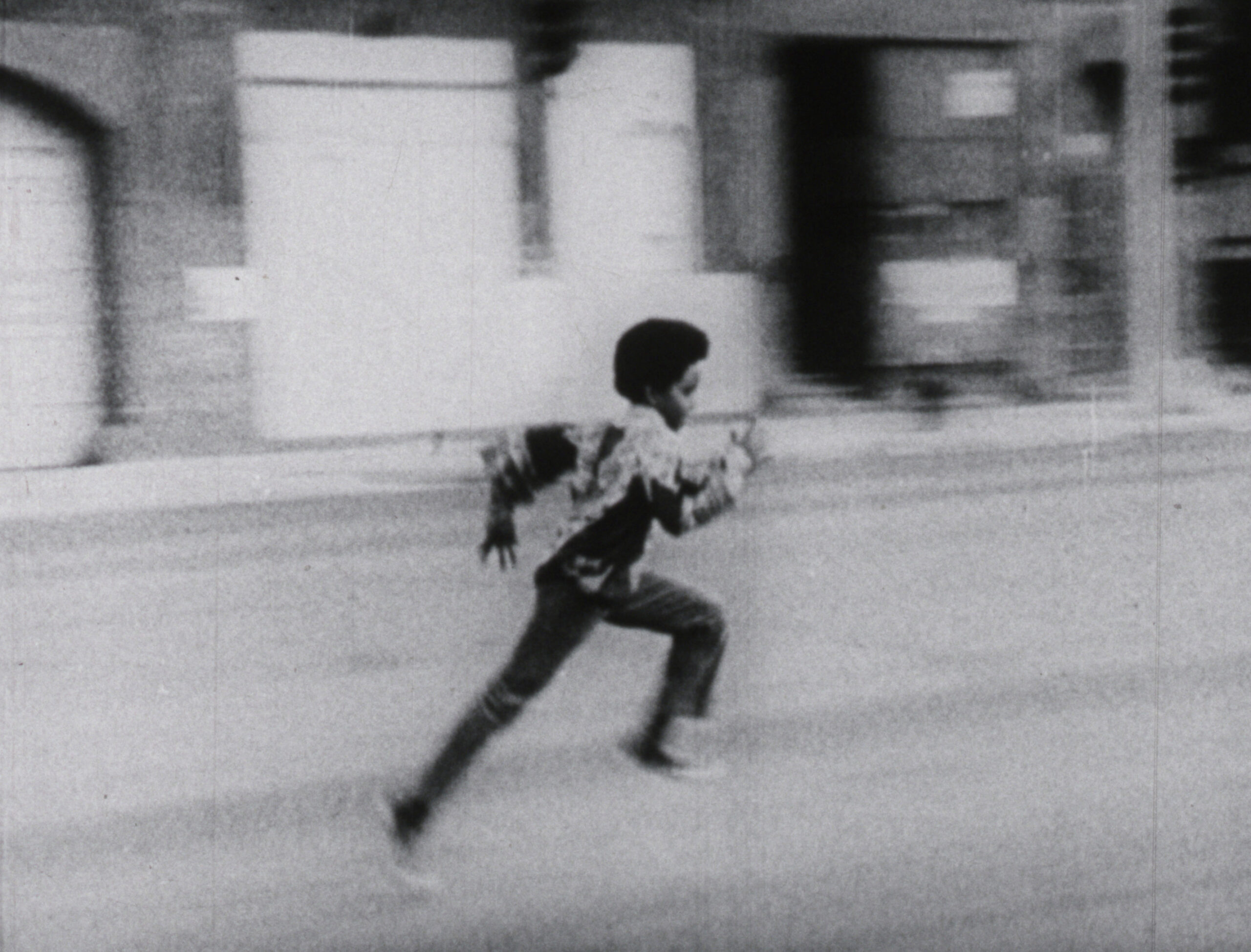 A black and white film still from We Are Universal of a kid running through a city street.